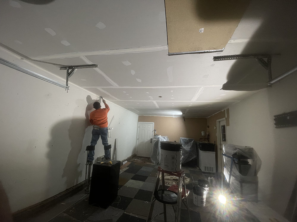 Finisher on stilts taping perimeter ceiling joint near work lights